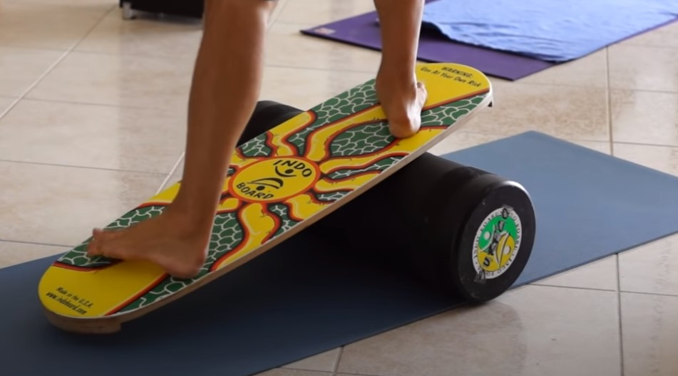 Barefoot person balancing on a vibrant Indo balance board on a blue yoga mat.