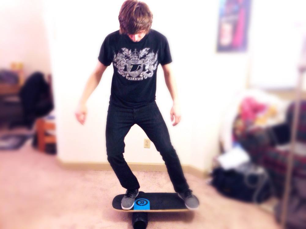 Young man in black shirt practices balance on a blue and black balance board.
