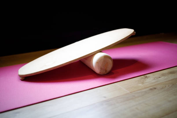 Natural wood balance board with roller on a pink yoga mat for training.