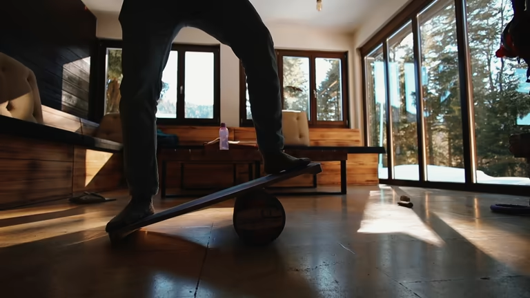 Person's legs on a wooden balance board indoors, training core balance in sunlight.