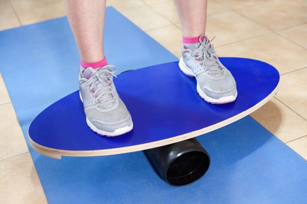Close-up of feet on a blue oval balance board with roller on a yoga mat.