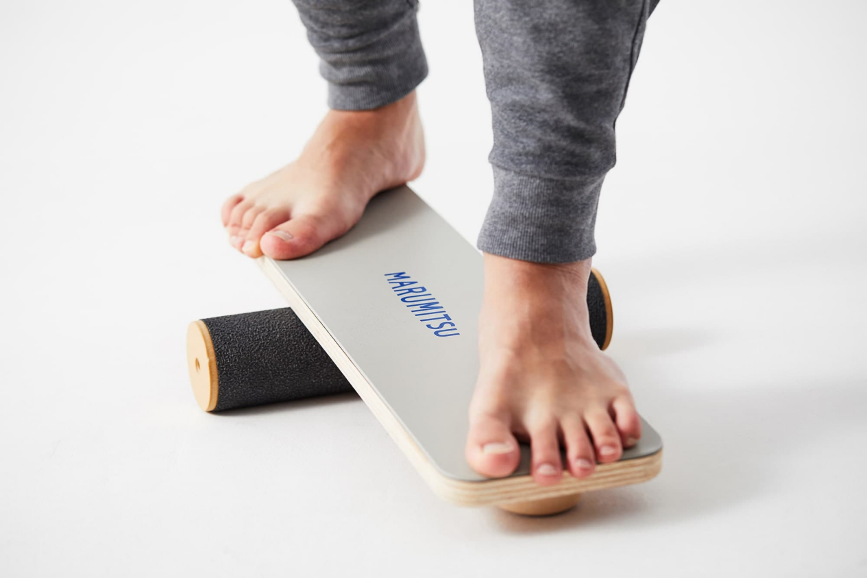 Person practicing on a grey balance board with 'MARUMITSU' text.