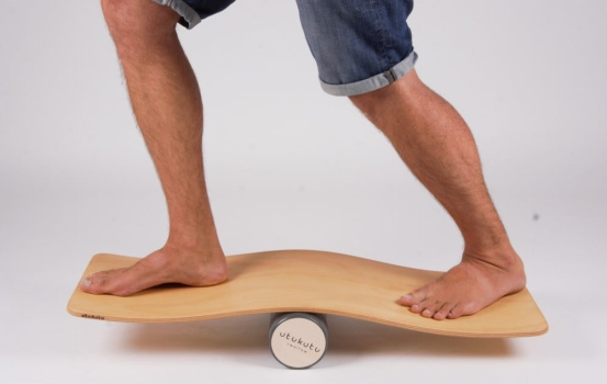 Man balancing on a curved wooden balance board with roller.