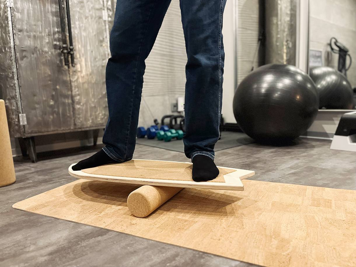 Person in jeans and socks stands on a cork and wood balance board.