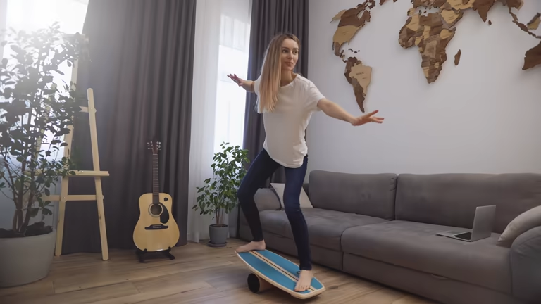 Barefoot woman training core strength on a balance board in a bright living room.