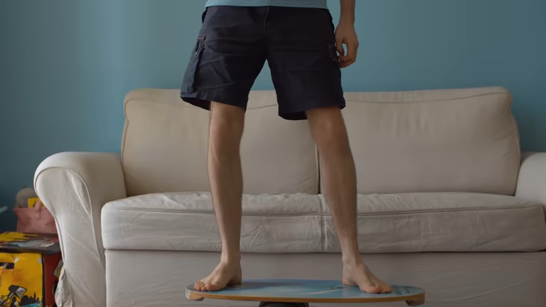 Person standing barefoot on a wooden balance board indoors in a living room.